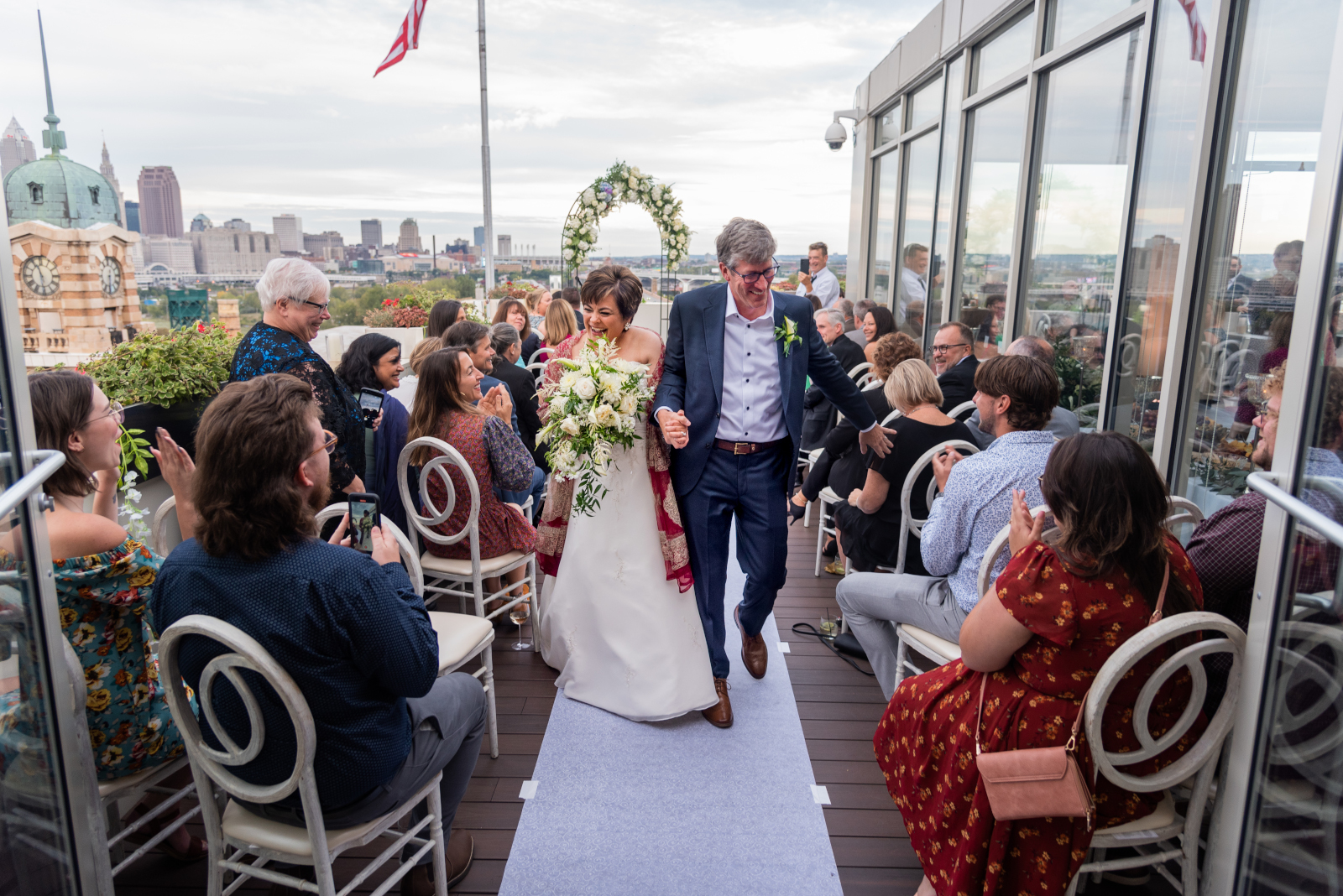 Bride and groom walking down the aisle, bridal recessional, wedding ceremony, smiling, laughing, sweet, cute, older couple, romantic outdoor urban wedding ceremony at Penthouse Events, Ohio City, Cleveland Flats, downtown Cleveland skyline, West Side Market, Lake Erie