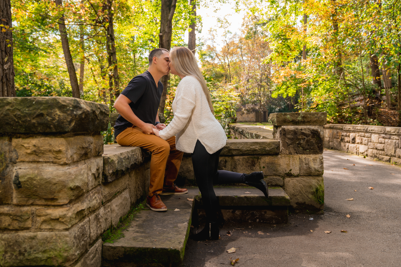Man and woman fiancee engagement photo, couple portrait, kiss, bench, stone, fall leaves, fall colors, trees, nature, outdoor fall engagement photo session at Grand Pacific Junction Historic Shopping District