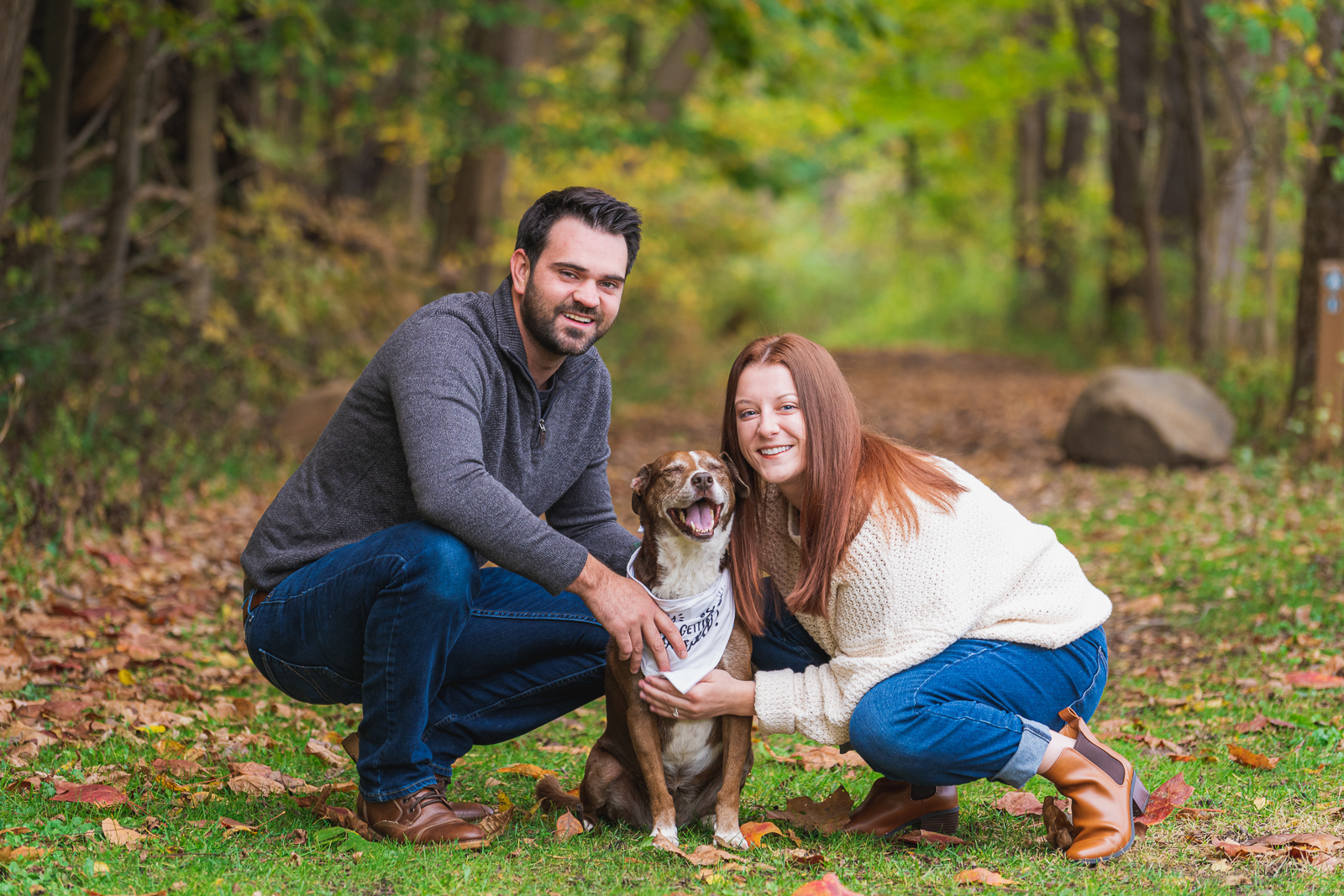 Man and woman fiancee engagement photo with dog, smile, cute dog, dog bandana, outdoor, nature, forest, fall leaves, fall colors, outdoor fall engagement photo session at Tinkers Creek, Bedford Reservation, Cleveland Metroparks